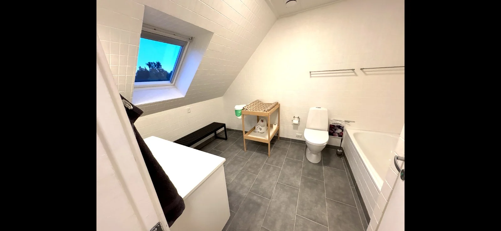 Badeværelse med badekar, toilet, håndvask og ovenlysvindue